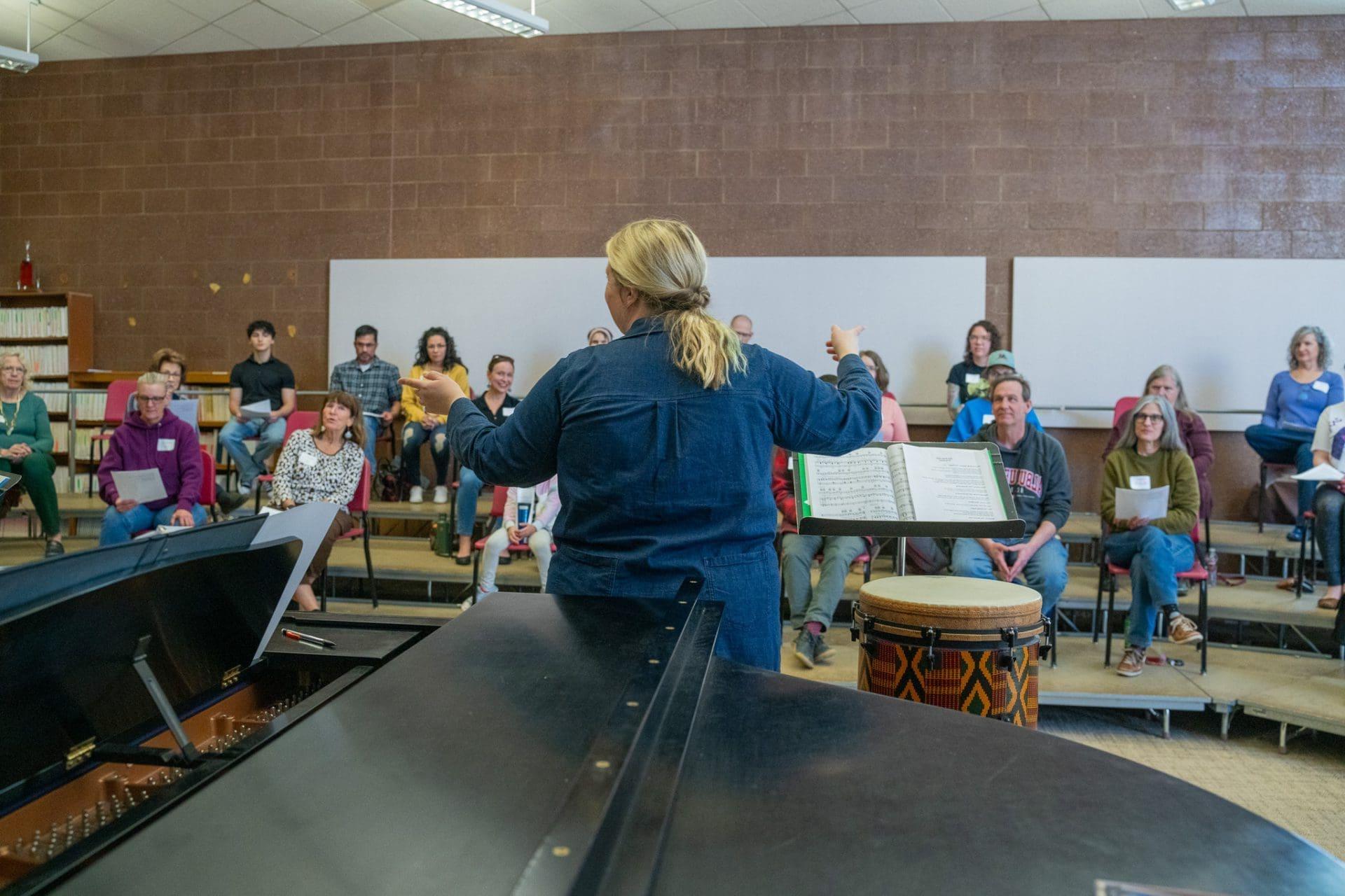 Choir director leading group rehearsal with piano.